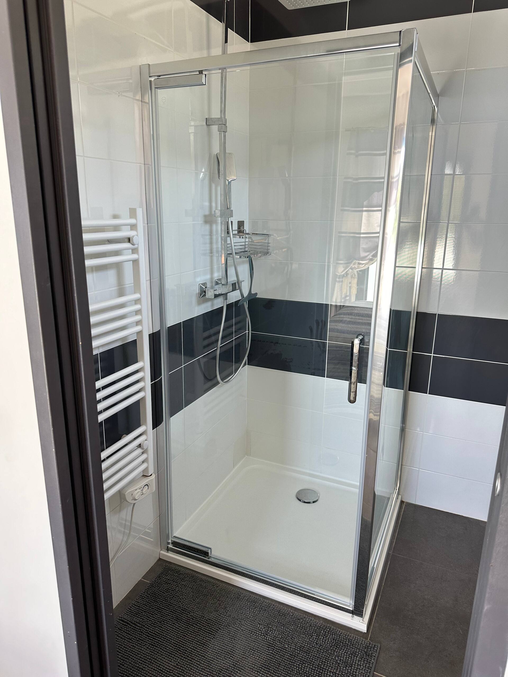 Douche vitrée et sèche-serviettes dans une salle d’eau carrelée