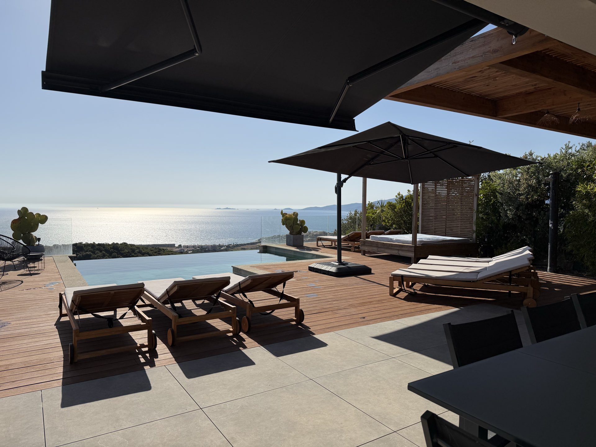 Bains de soleil alignés sur la terrasse en bois, la mer scintillante au fond