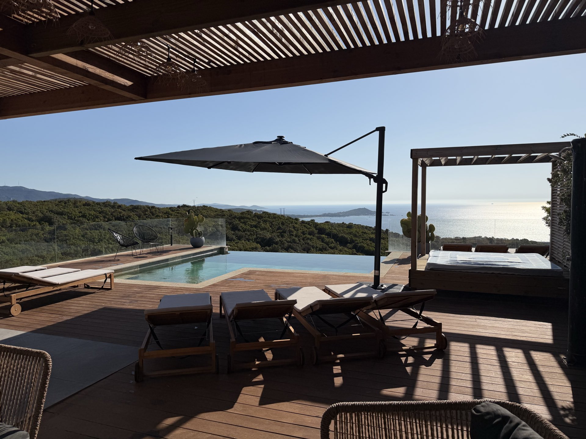 La piscine et le lit de repos couvert, vus depuis le salon d’extérieur abrité par la pergola