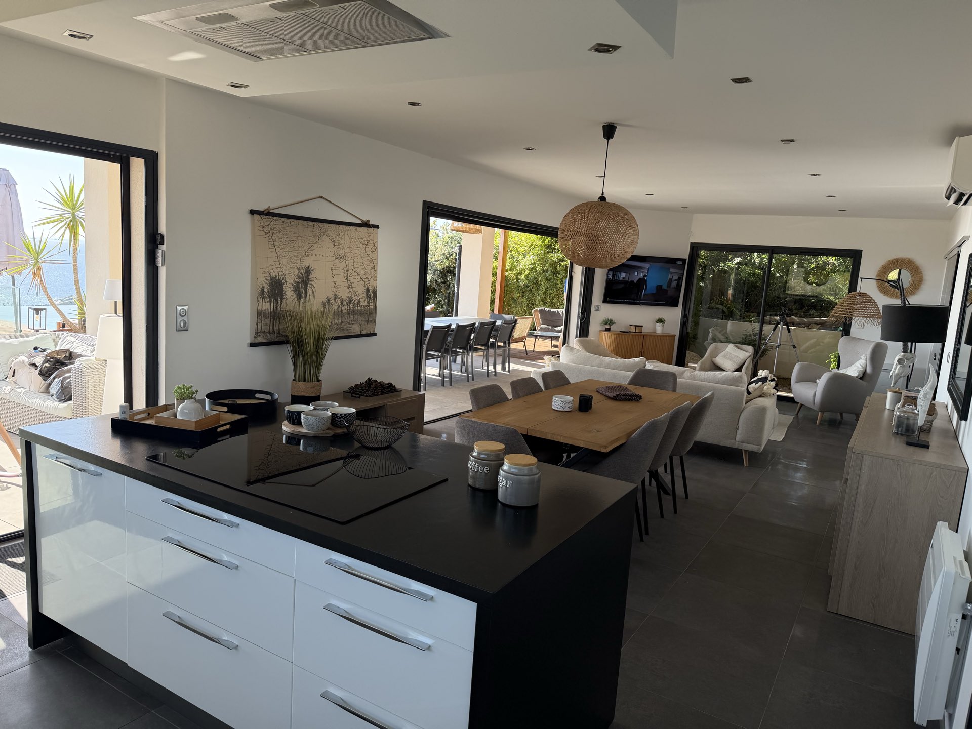 La table et le séjour depuis la cuisine, les baies ouvertes sur la terrasse et la piscine