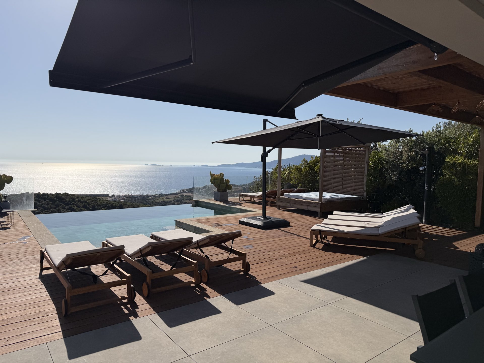La terrasse en bois et ses bains de soleil au bord de la piscine à débordement, ouverte sur tout le golfe