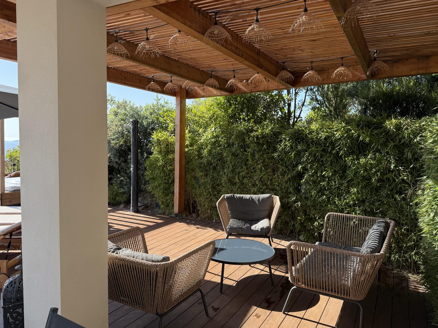 Fauteuils en corde tressée sous la pergola, guirlande de lampions et haie de bambous