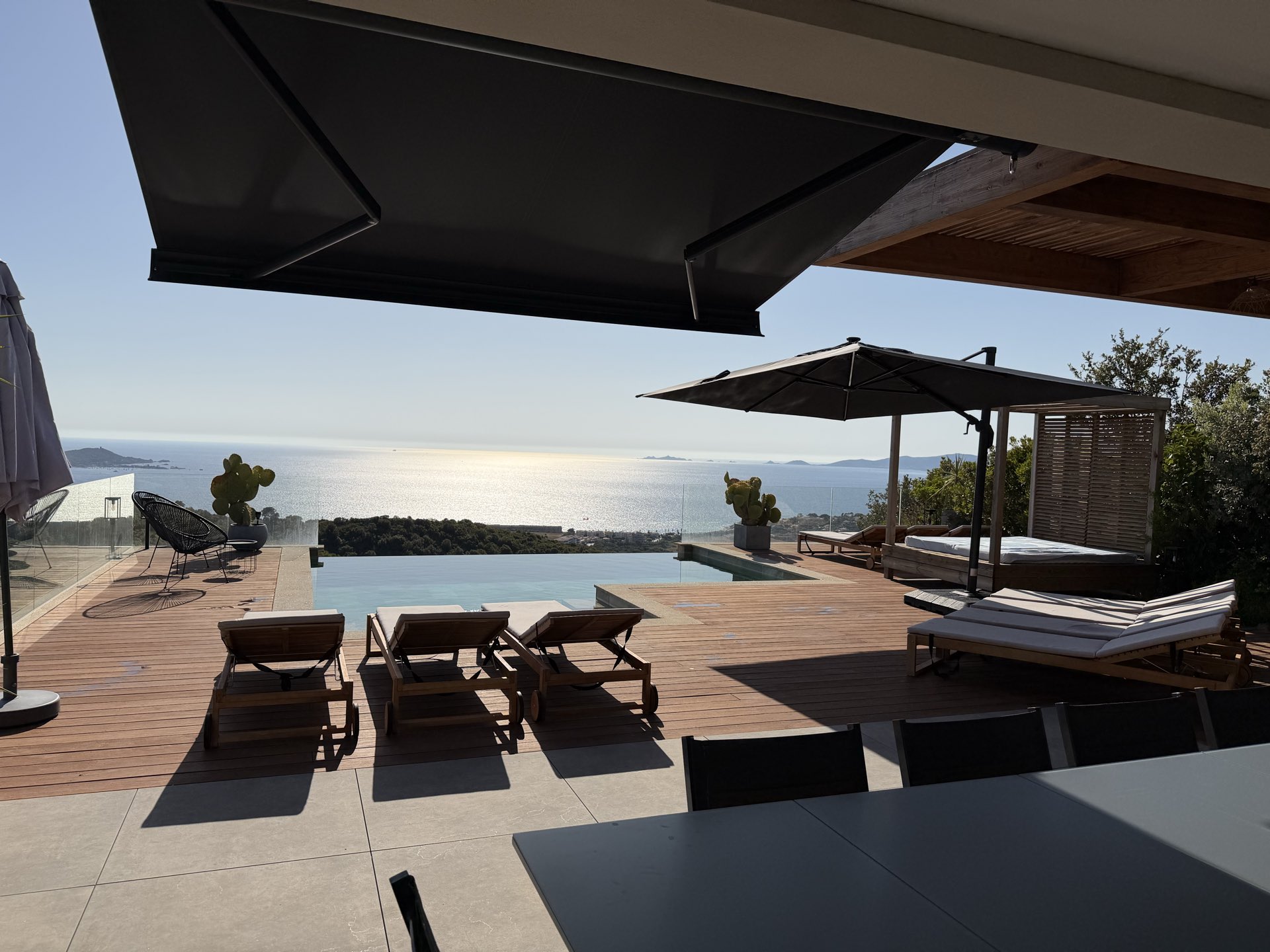 La grande table de repas sur la terrasse, la piscine à débordement et la mer derrière